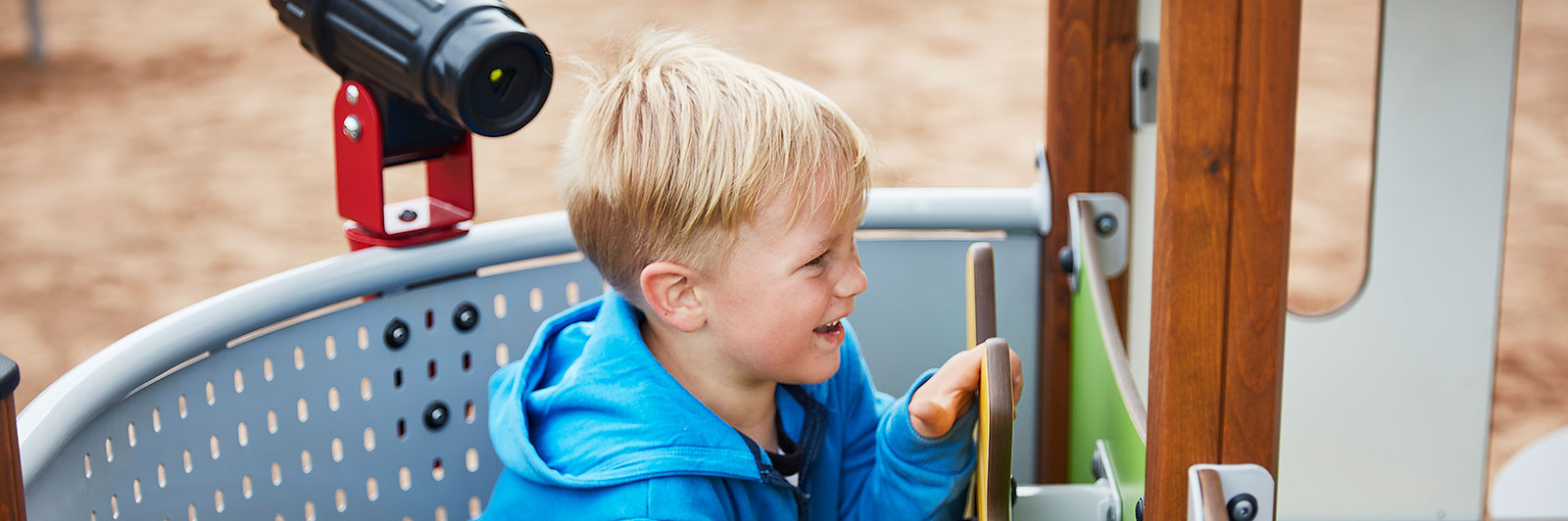 A young boy interacts with play panels from within a playground unit which has a playhouse built in.